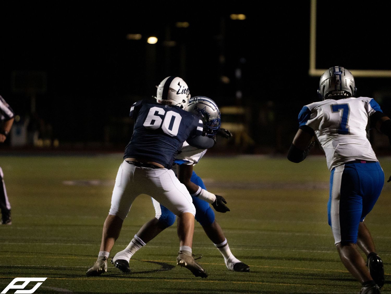 Player number 60 blocks opponent during intense night football game action.