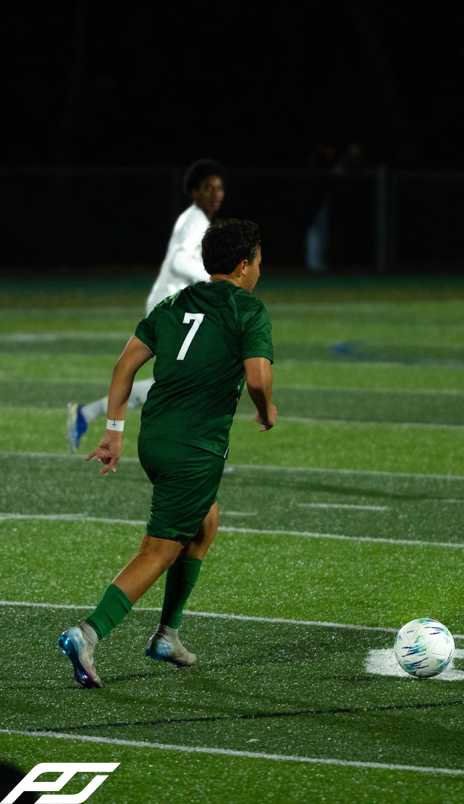 Soccer player #7 in green uniform controls the ball on a turf field during a nighttime match.