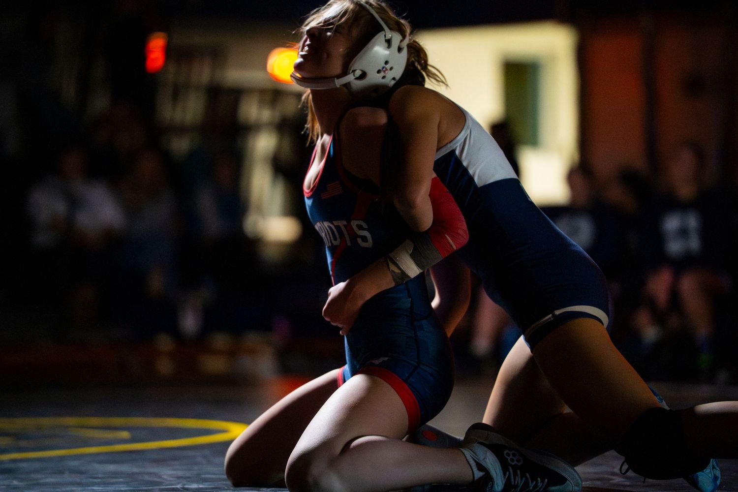 Two female wrestlers grapple in close combat during an intense indoor wrestling match.