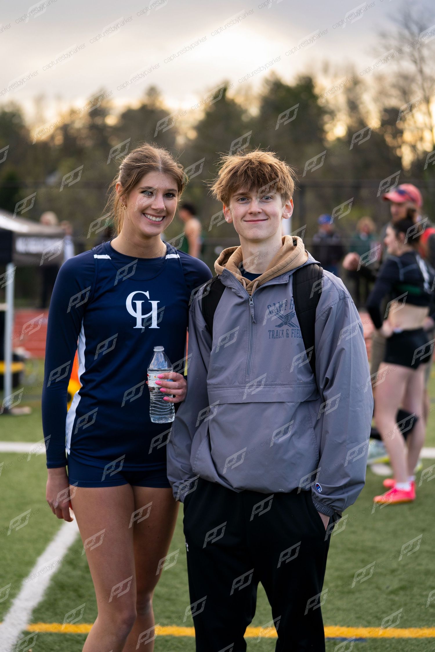 Female CH track athlete and male student pose together smiling at outdoor track meet.