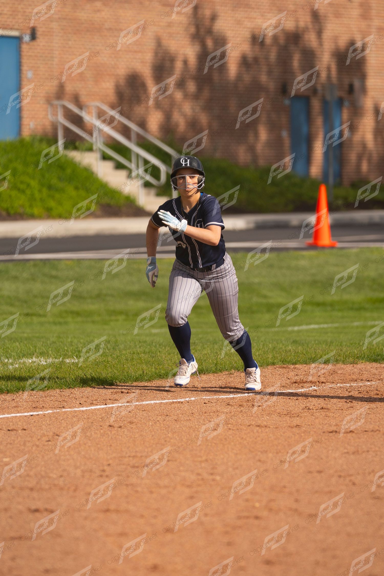 Female softball player in navy pinstripe uniform takes a lead off base during a softball game.