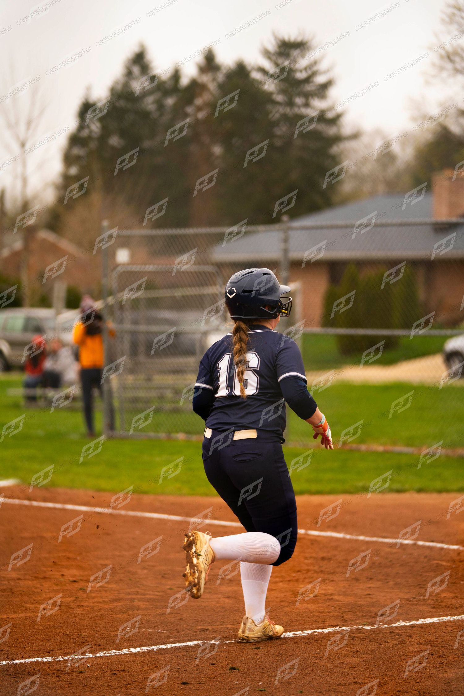 Female softball player #16 in navy uniform runs the baseline during an outdoor game.
