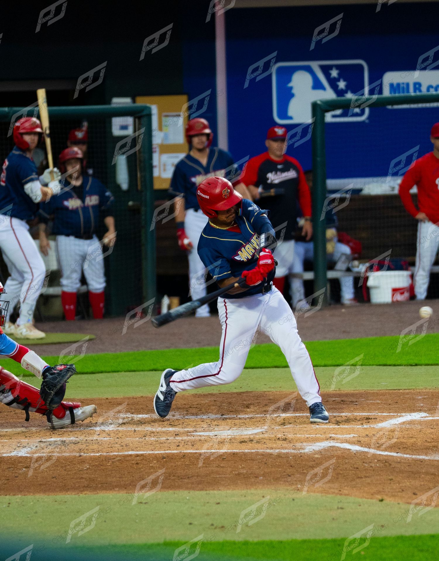 Baseball batter swings at pitch during night game while catcher and umpire watch at home plate.