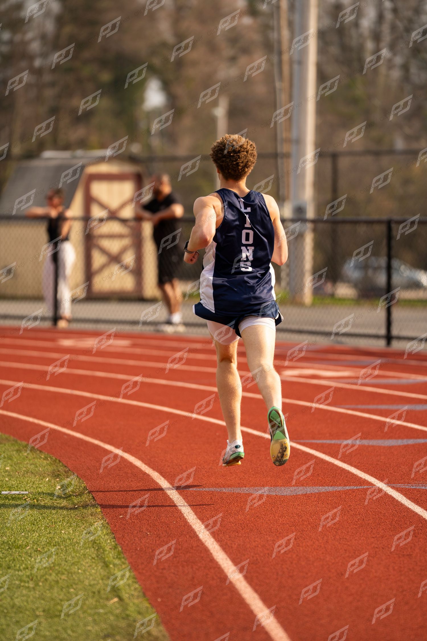 Rear view of Lions track runner in navy uniform racing on red outdoor track.