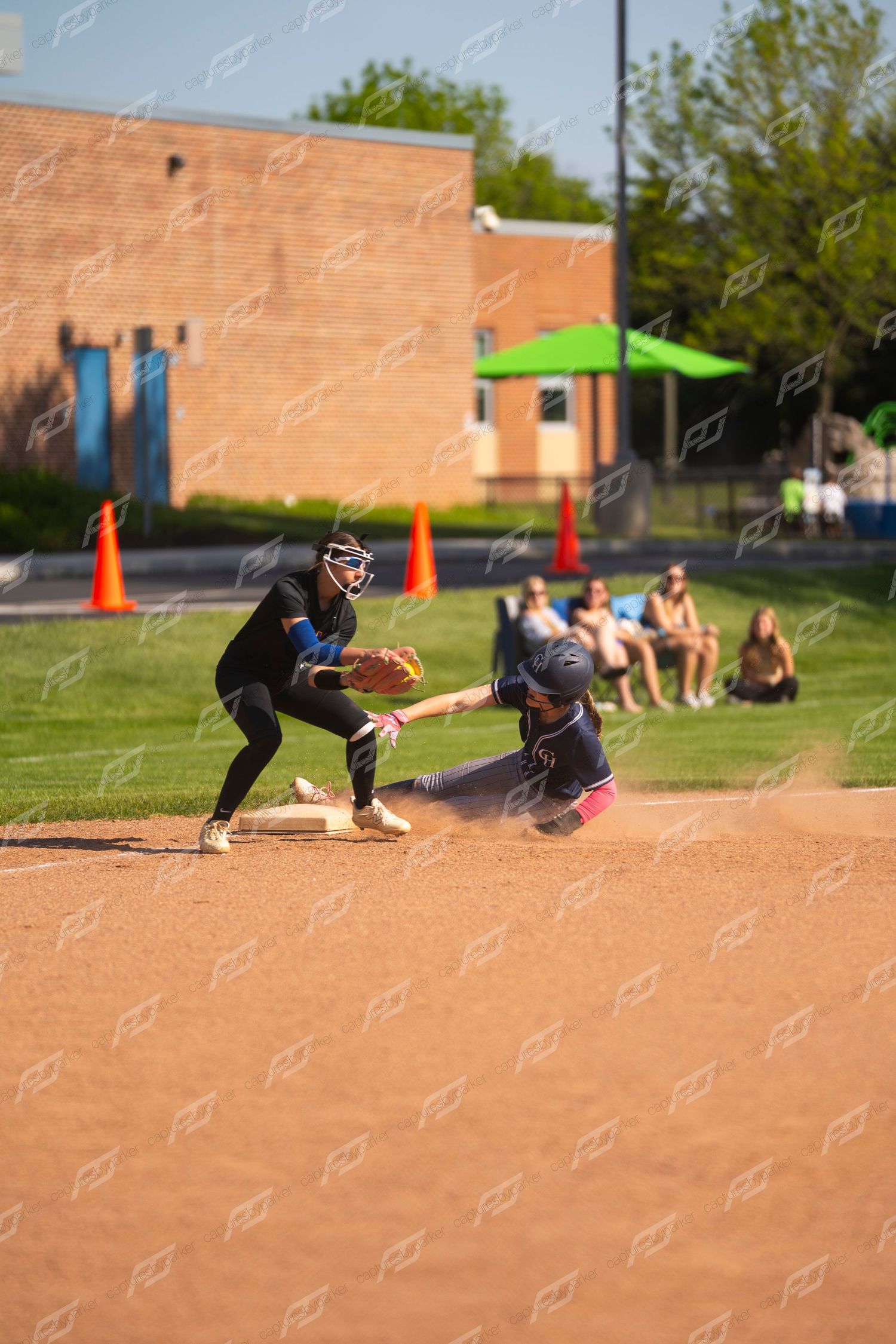 Softball player slides into base as fielder attempts a tag during an outdoor game.