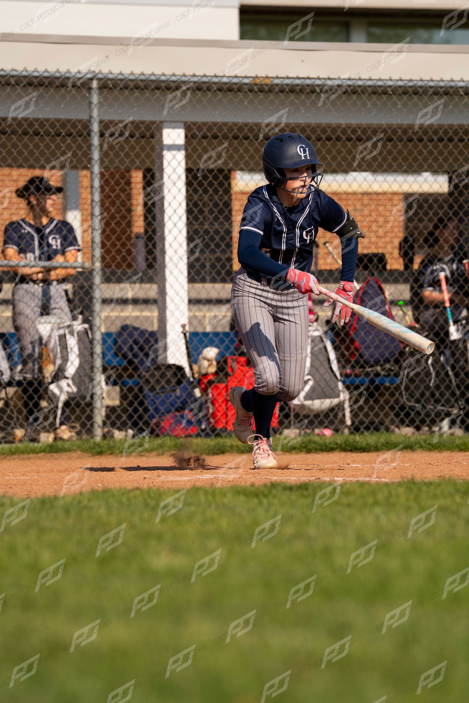 Female softball player in navy pinstripe uniform following through on a swing during a softball game.