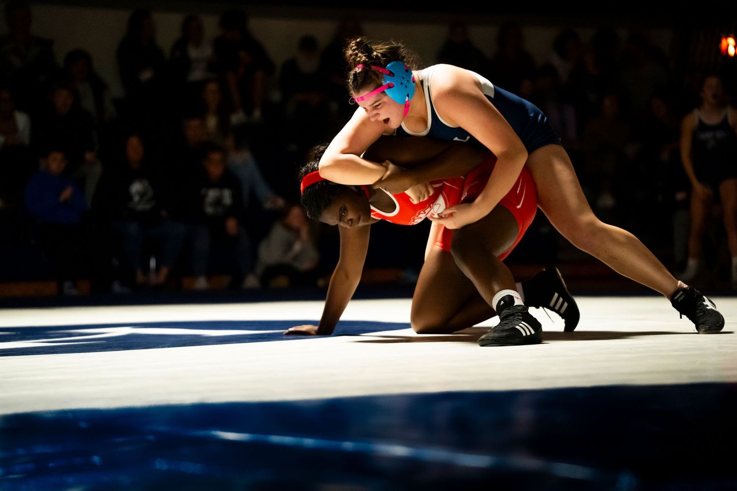 A blue-uniformed wrestler takes down an opponent during a high school wrestling competition.