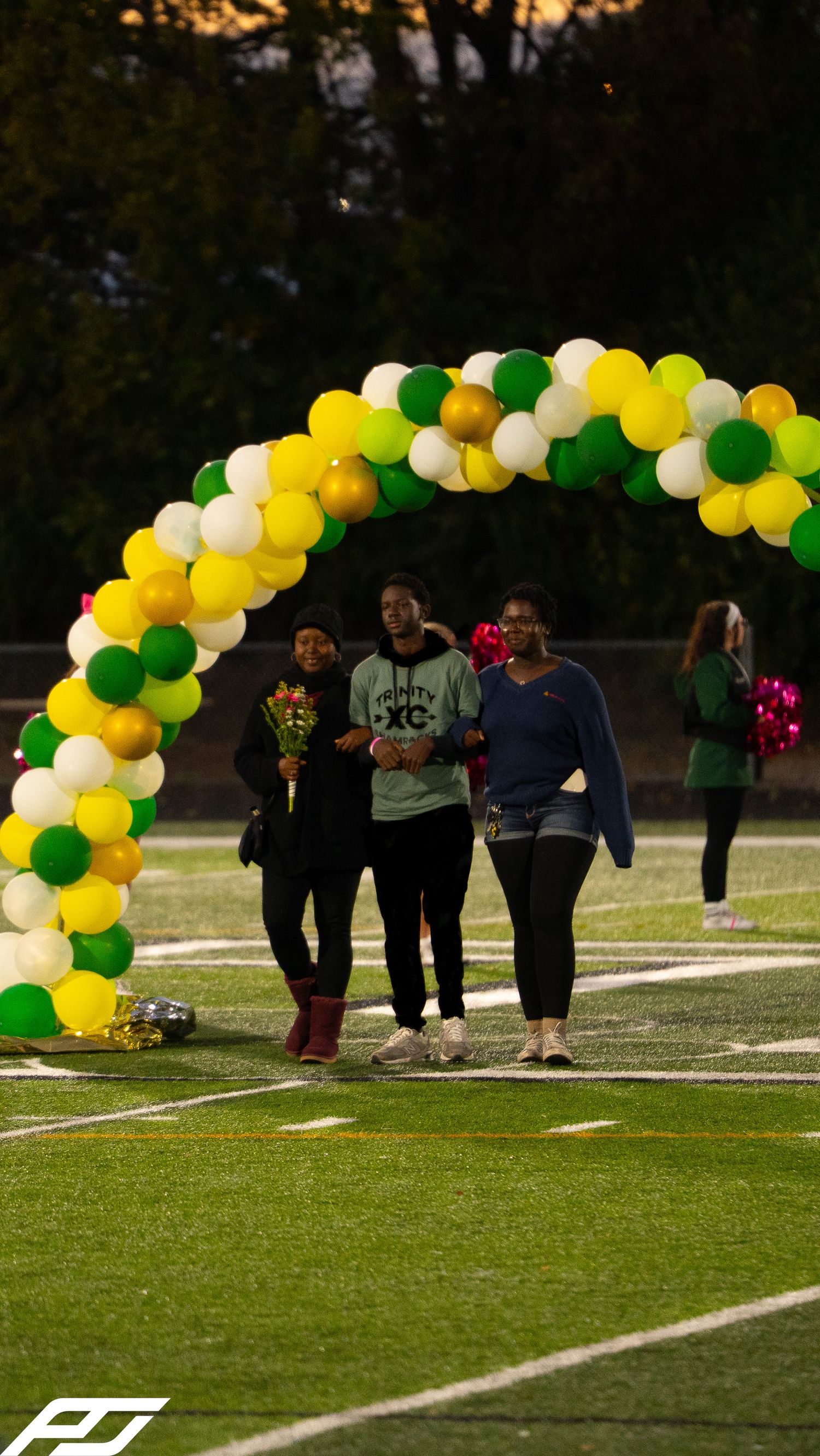 Student in Shamrocks cross country gear walks with two family members under balloon arch at senior night.