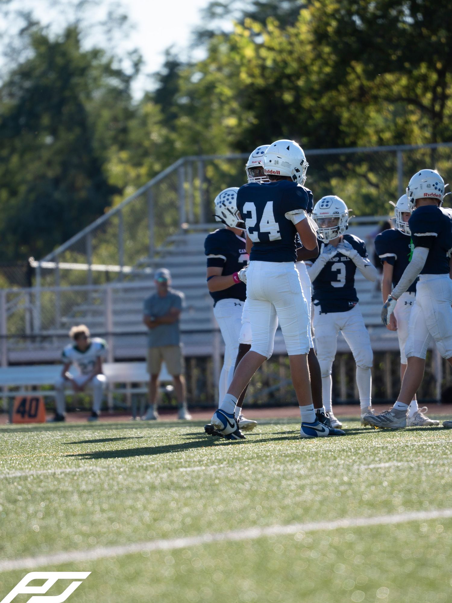 Two Camp Hill football players #24 and #3 huddle on field in white helmets and uniforms.
