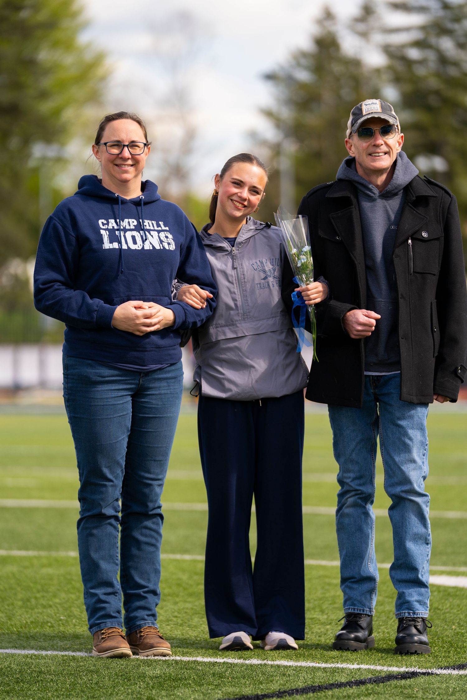 Three people smile together on a football field during a school senior day recognition event.