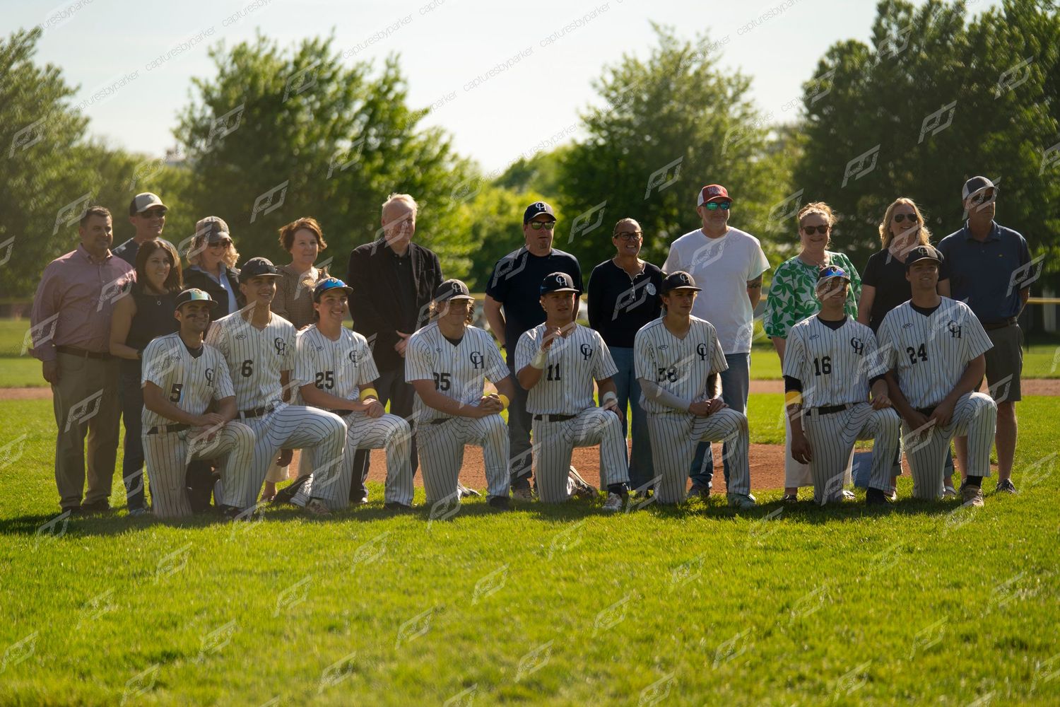 High school baseball team poses with parents and coaches for a group photo on a sunny green field.