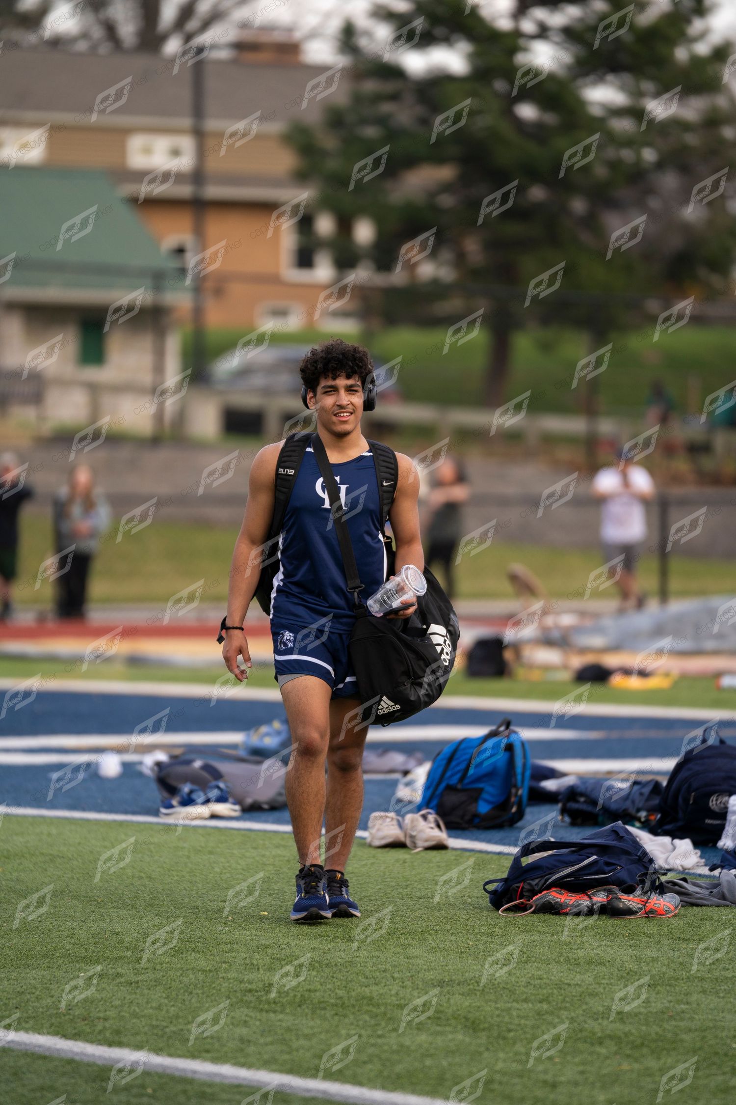Smiling male track athlete carries gear bag on blue turf field.