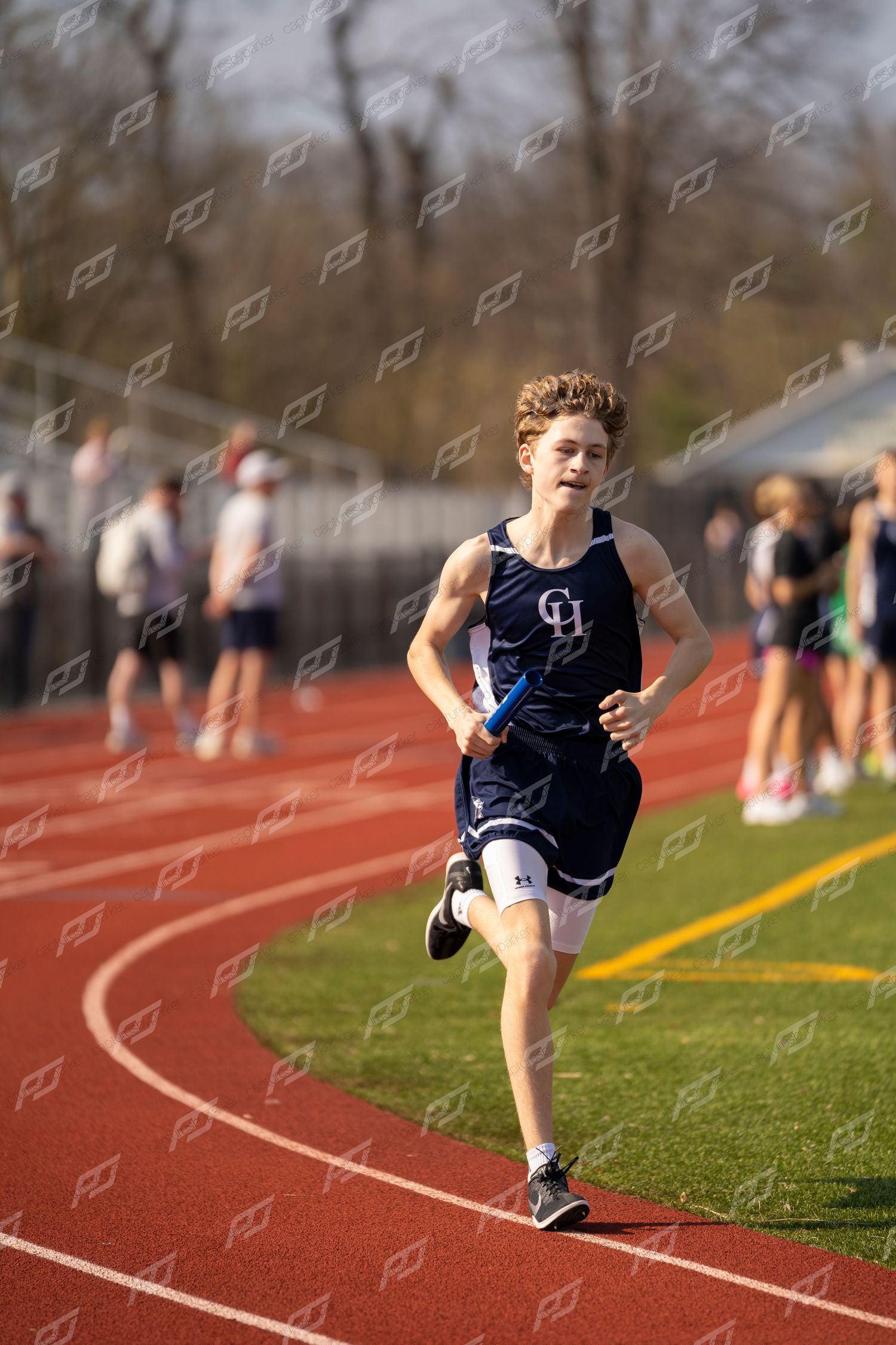 Young male runner in navy uniform competing on red outdoor track during a field meet.