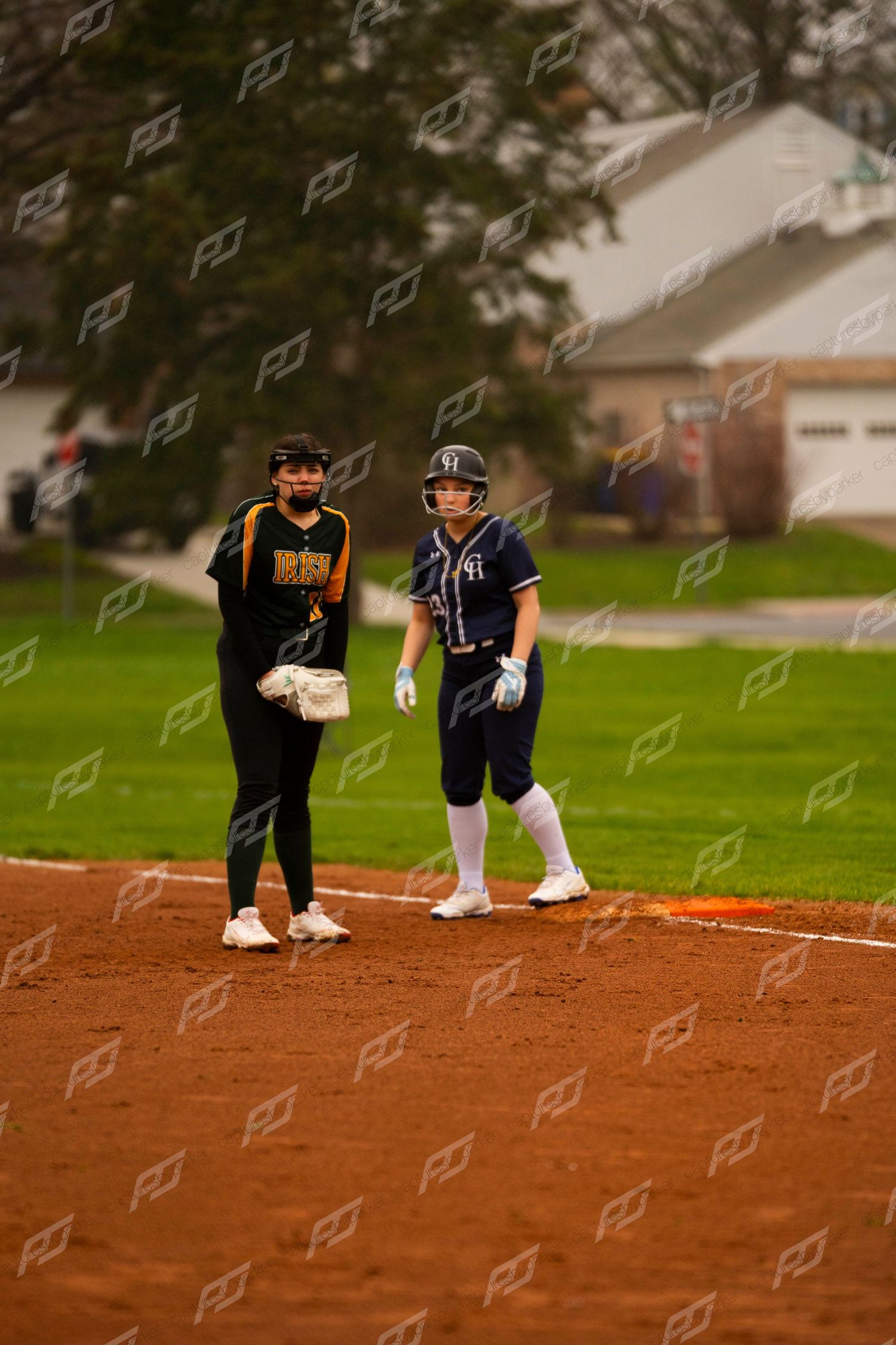 Two softball players stand at base, one in navy uniform and one in black during game.