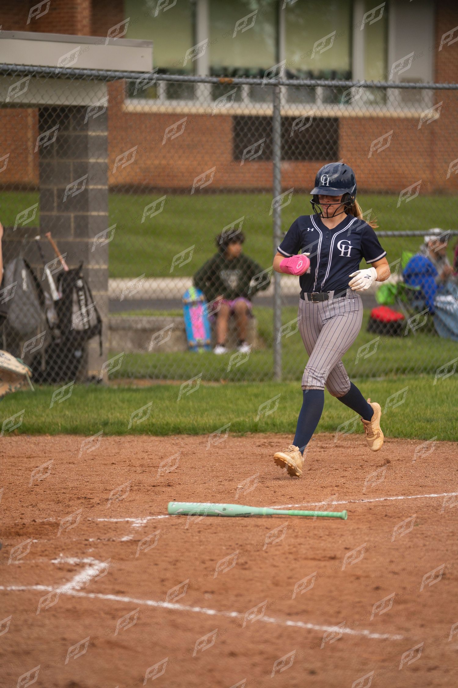 Softball player in navy uniform runs toward home plate during an outdoor game.