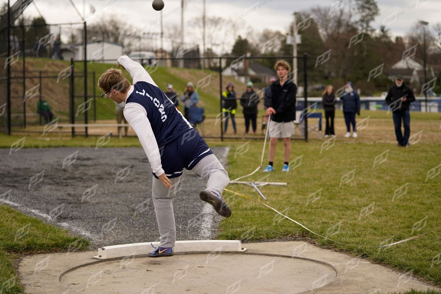 Male high school athlete spins to release a discus throw during an outdoor track and field competition.