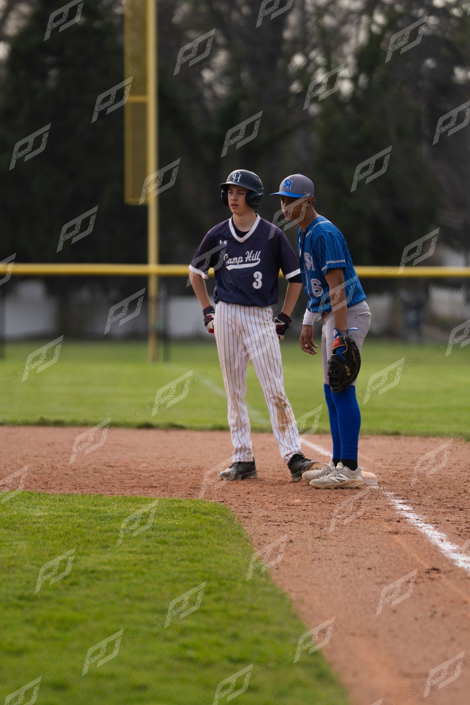 Baseball player #3 in navy pinstripe uniform stands at first base alongside opposing team coach during game.