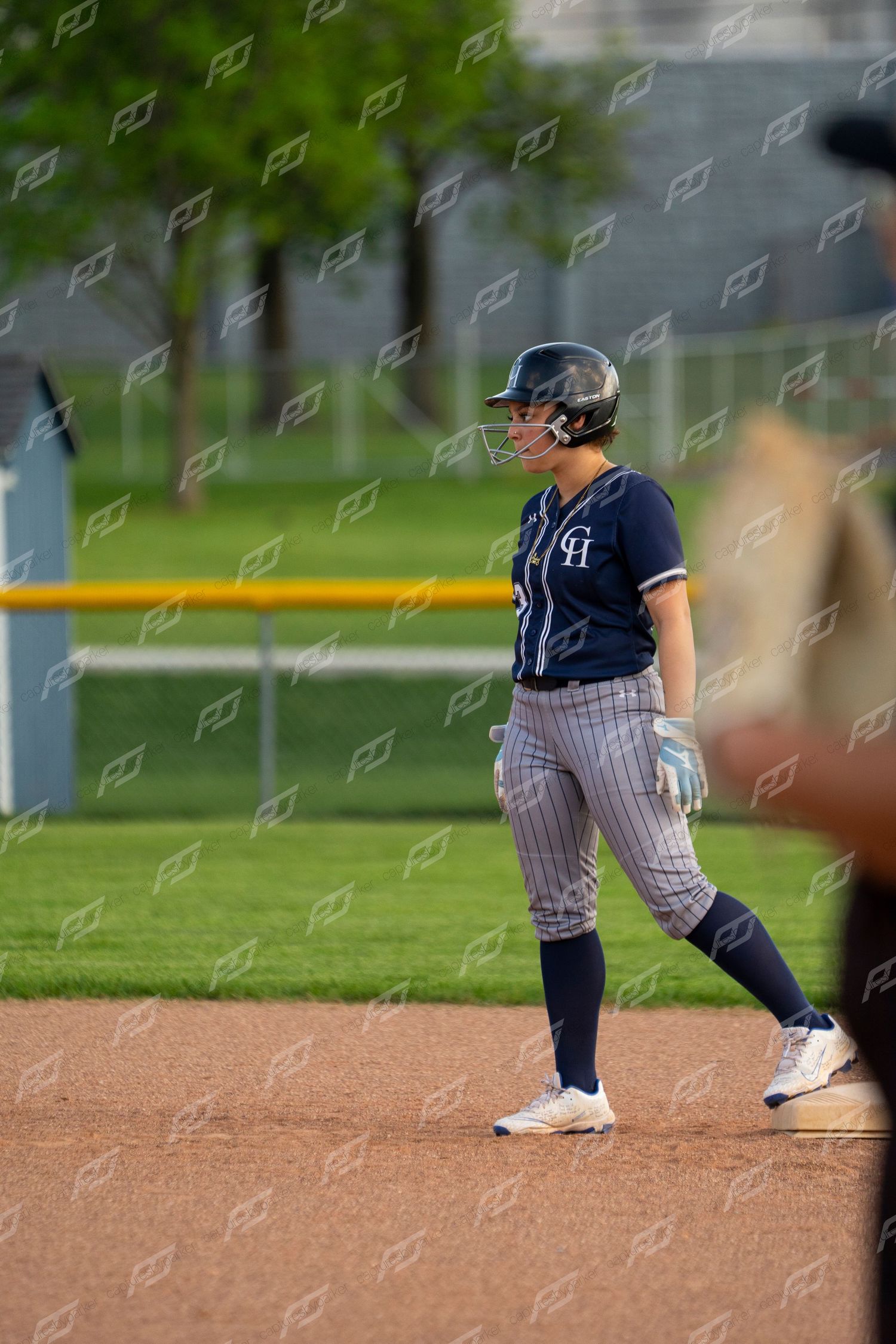 Female softball player in navy CH pinstripe uniform stands alert on base during a game.