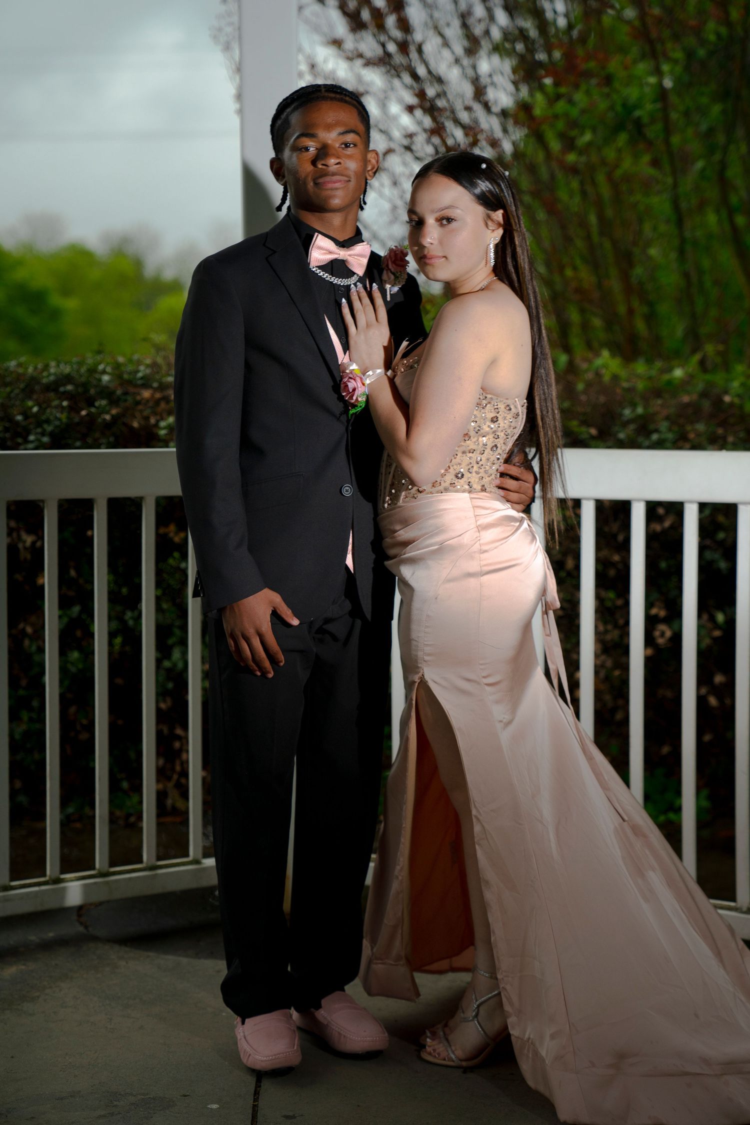 Prom couple poses together, young man in black tuxedo and woman in elegant blush pink gown.
