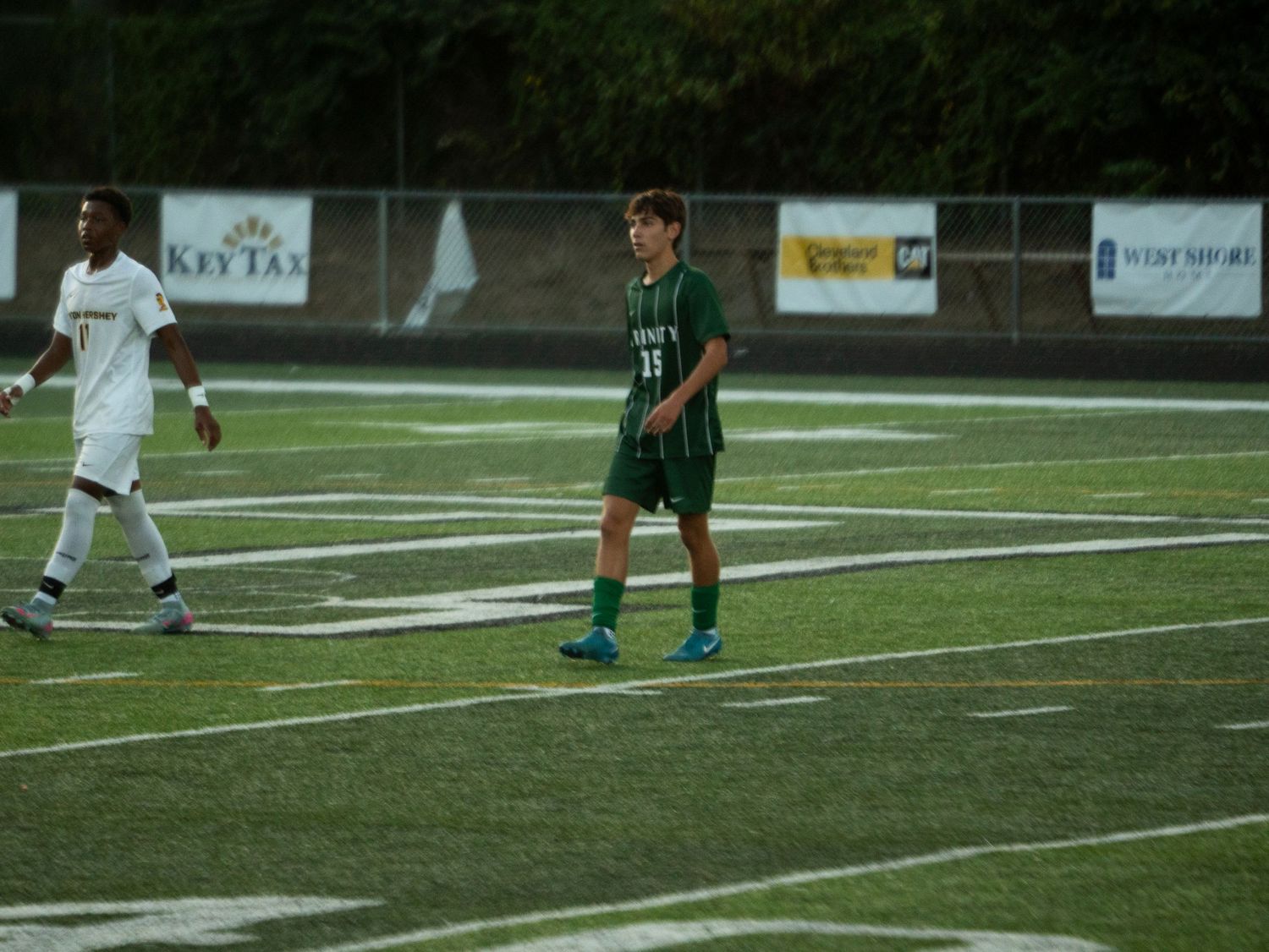 Youth soccer player wearing green number 11 jersey stands on artificial turf during a game.