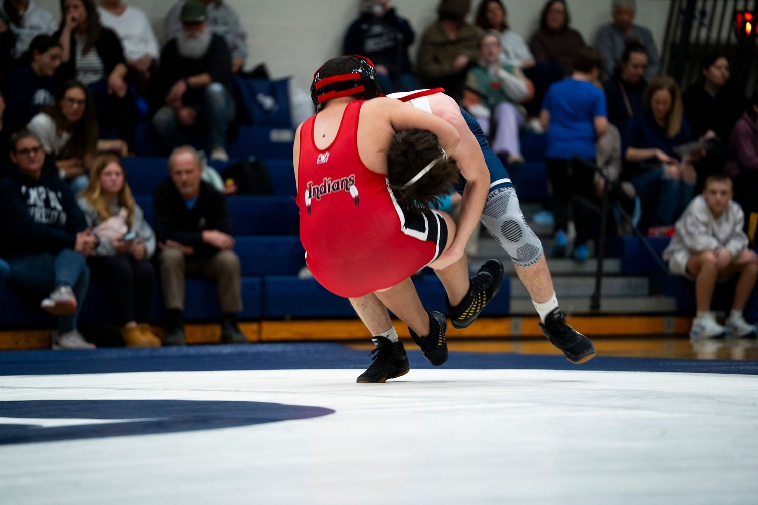 Wrestler in red singlet executes a dramatic throw during competitive high school wrestling match.