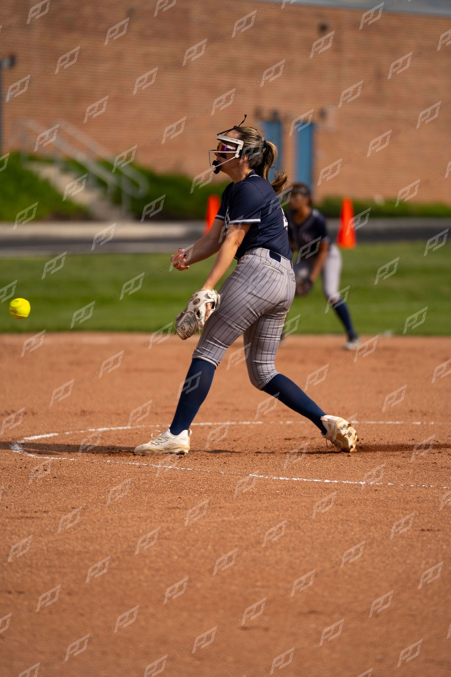Female softball pitcher releasing a yellow ball during a competitive softball game.