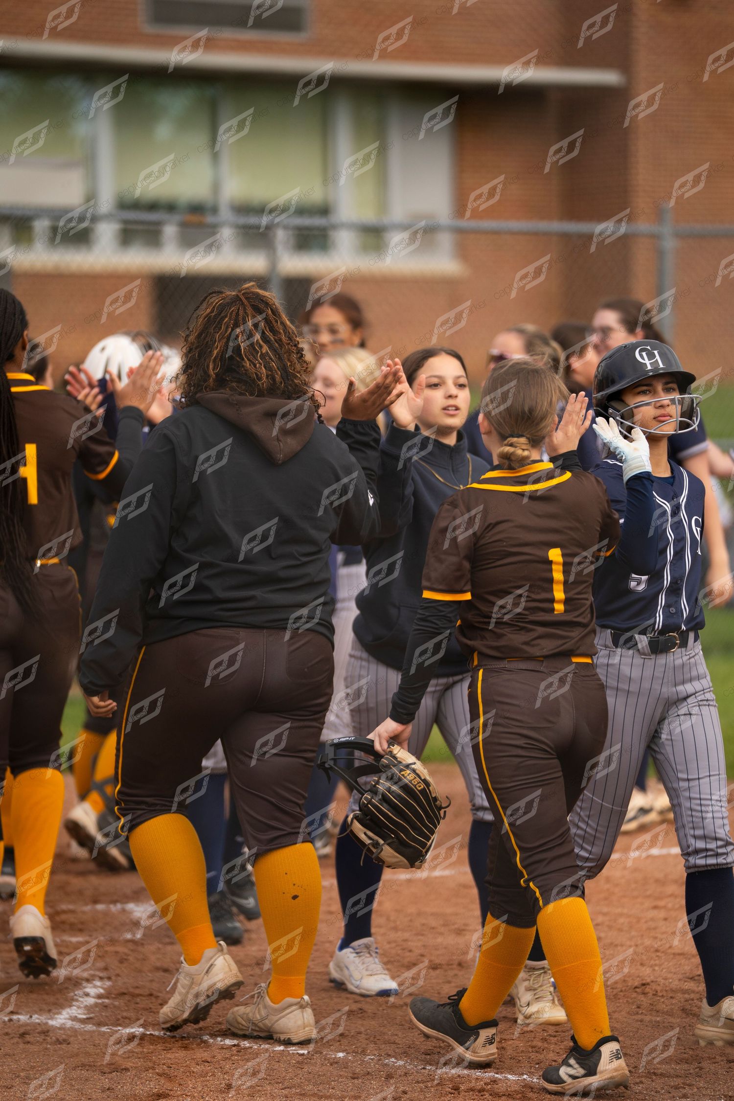 Softball players exchange high-fives in a post-game handshake line near home plate.