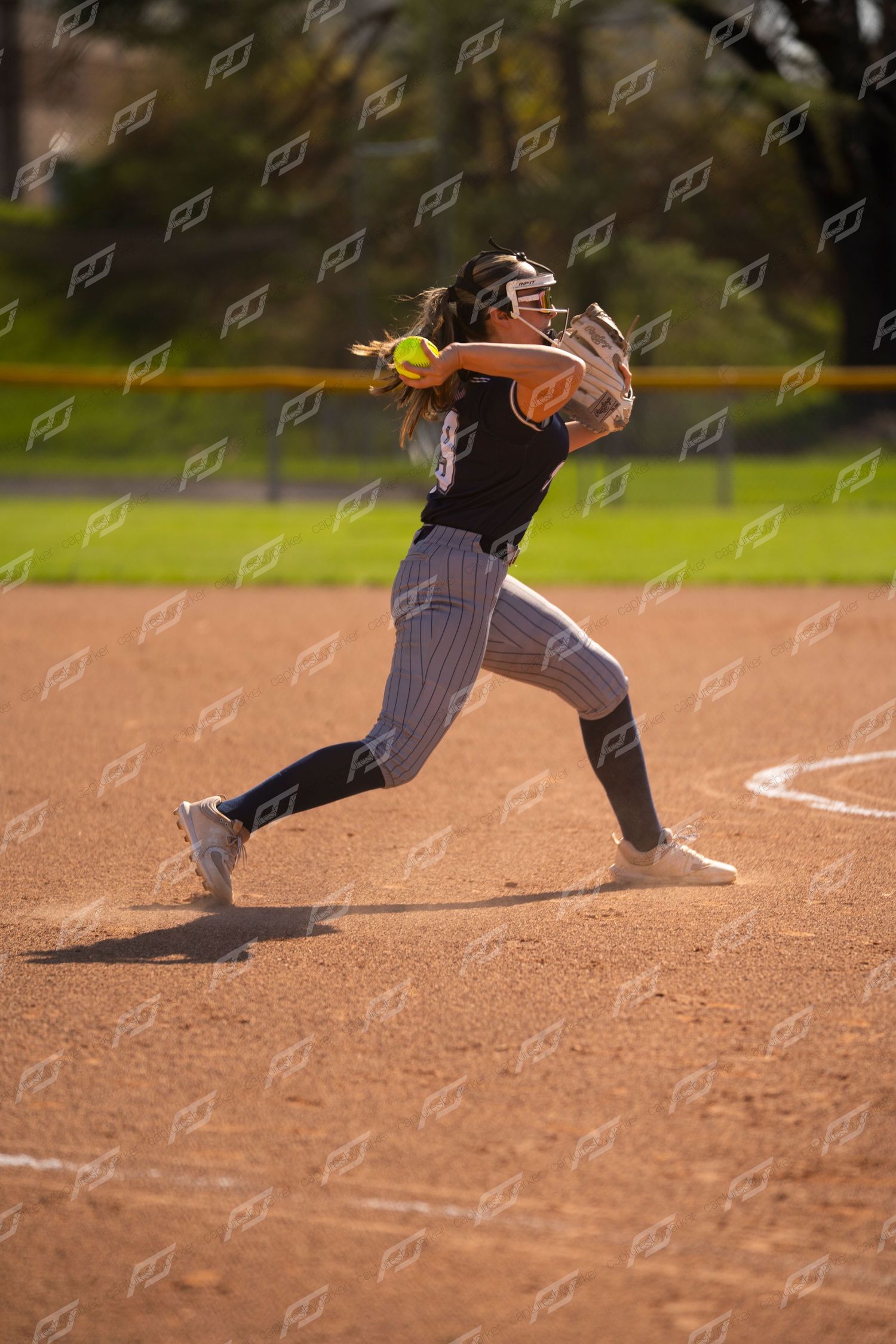 Softball pitcher in black pinstripe uniform delivers a pitch on the mound.