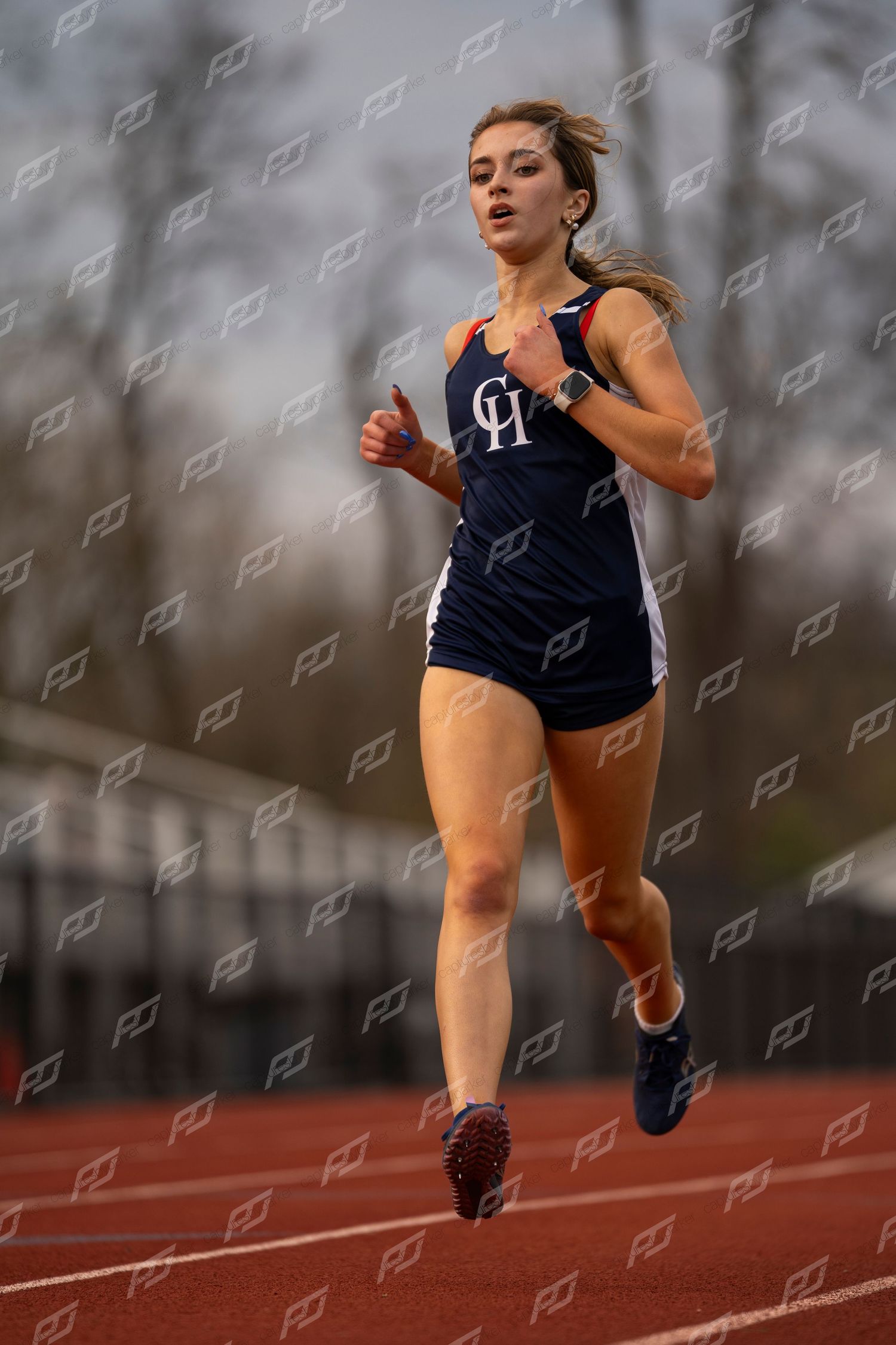 Female track athlete in navy CH uniform running on red track during competition.