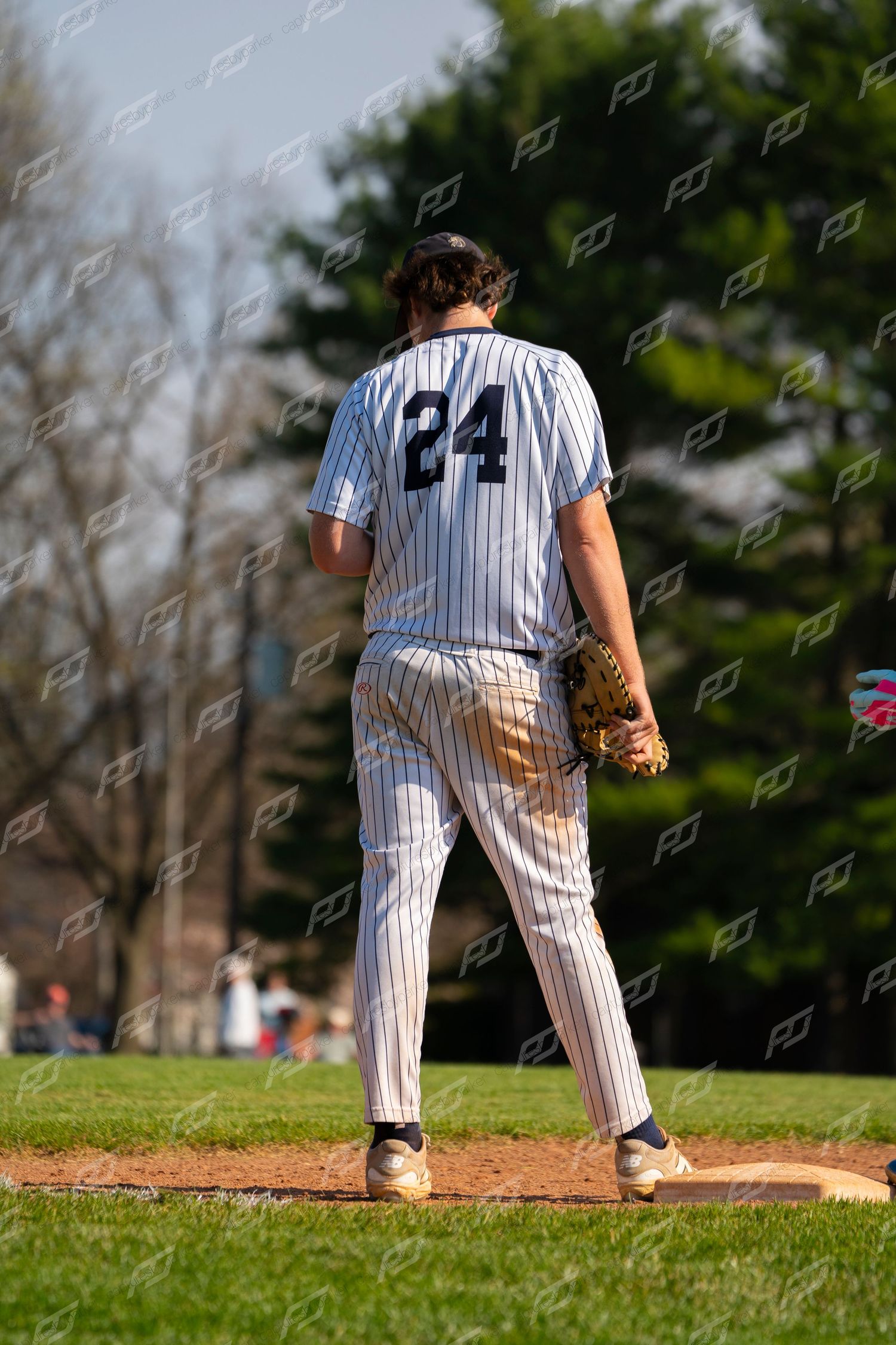 Baseball pitcher #24 in pinstripe uniform stands on mound viewed from behind on sunny day.