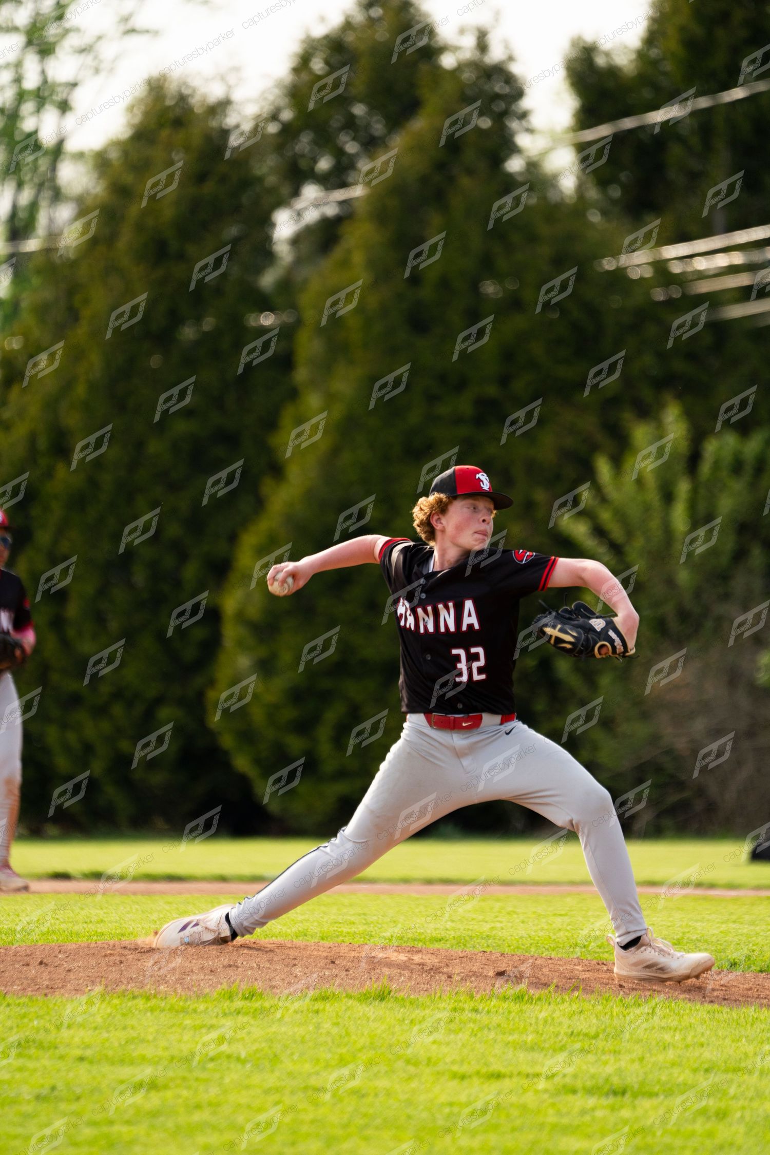 Baseball pitcher number 32 in black ANNA uniform winds up for a pitch on a sunny outdoor field.