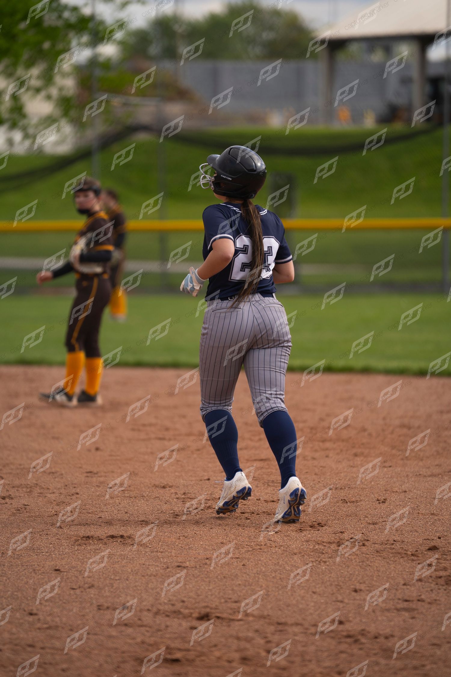 Female softball player #23 in navy uniform running the bases during a game.