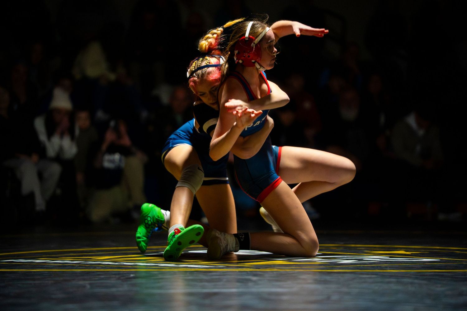 Two female wrestlers struggle in kneeling position during competitive wrestling tournament.