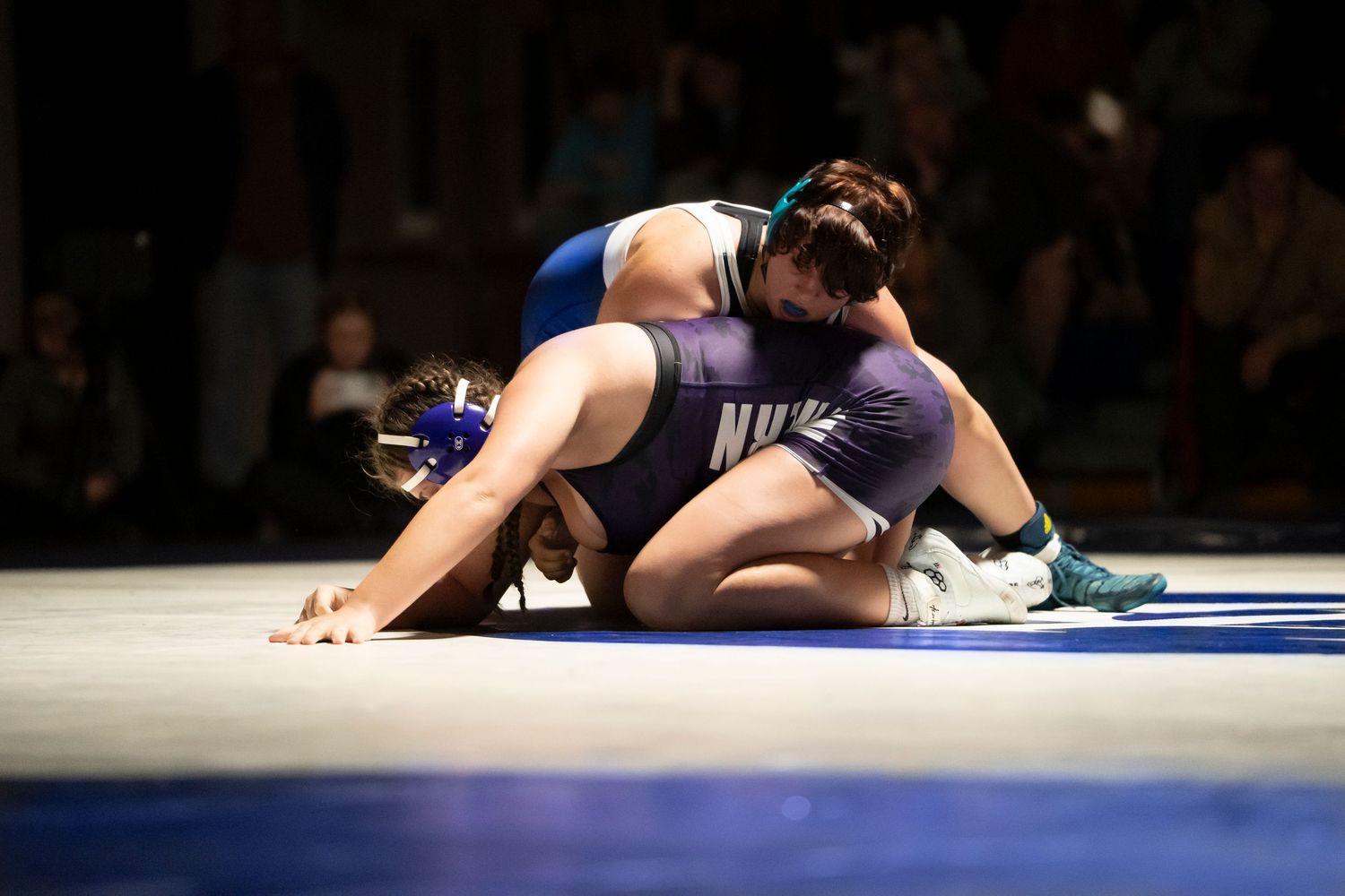 High school wrestler in blue singlet pins opponent to the mat during a competitive wrestling match.
