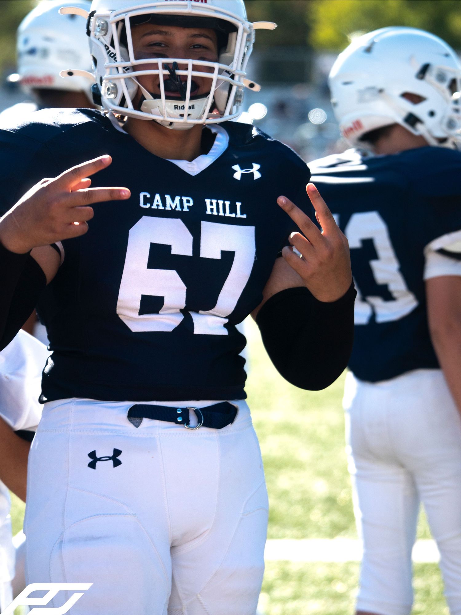 Camp Hill football player #67 poses in navy uniform and helmet on sunny game day.