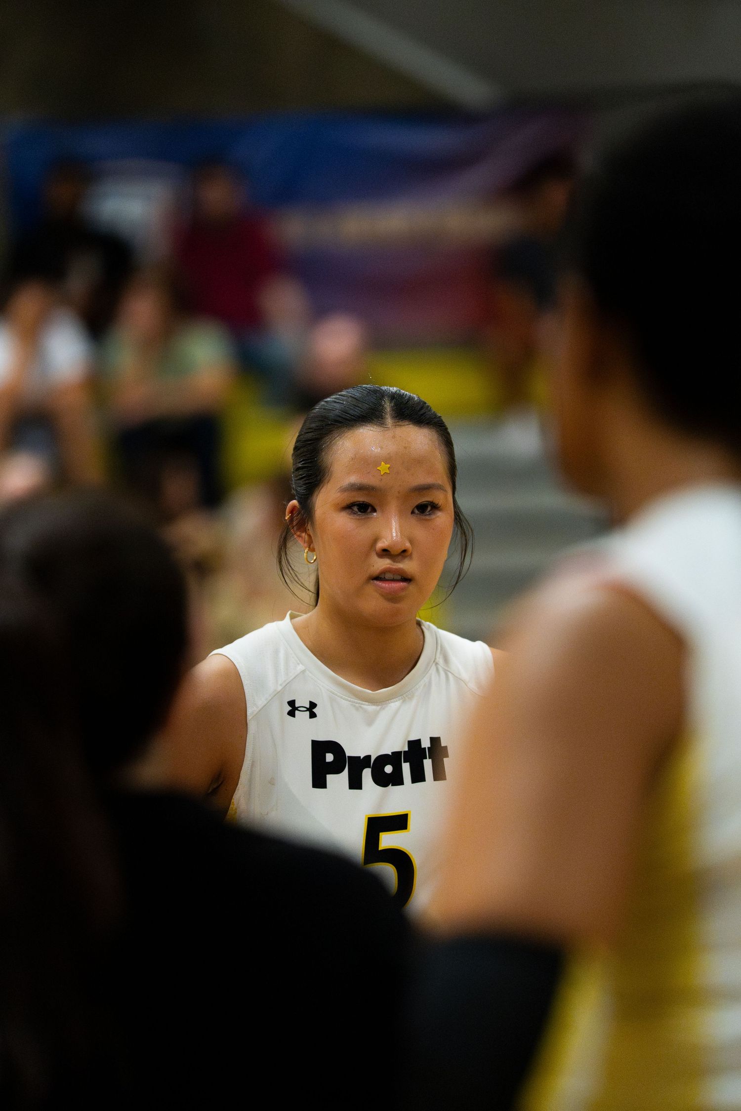 Female basketball player wearing Pratt number 5 jersey stands attentively during a game huddle.