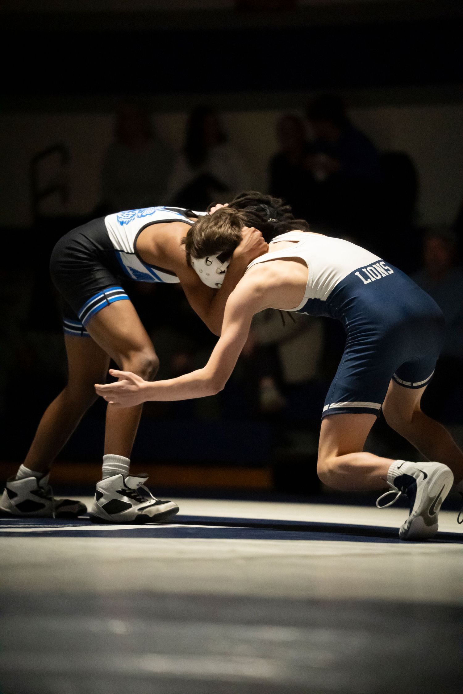 Two high school wrestlers engage in a tie-up stance on the mat during a competitive wrestling dual meet.