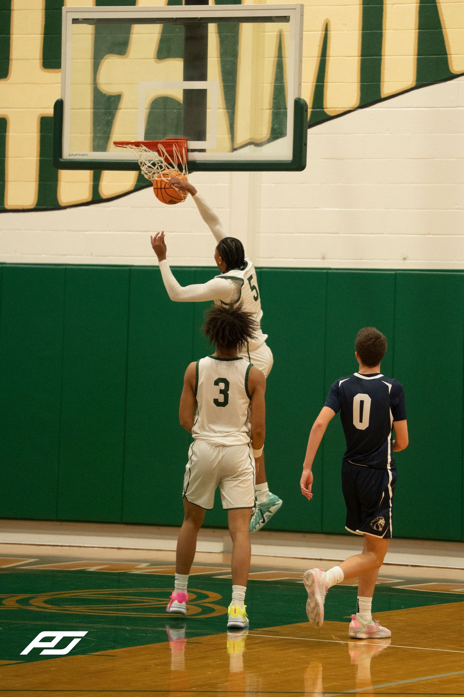 A basketball player dunks the ball during a high school game in a green gymnasium.