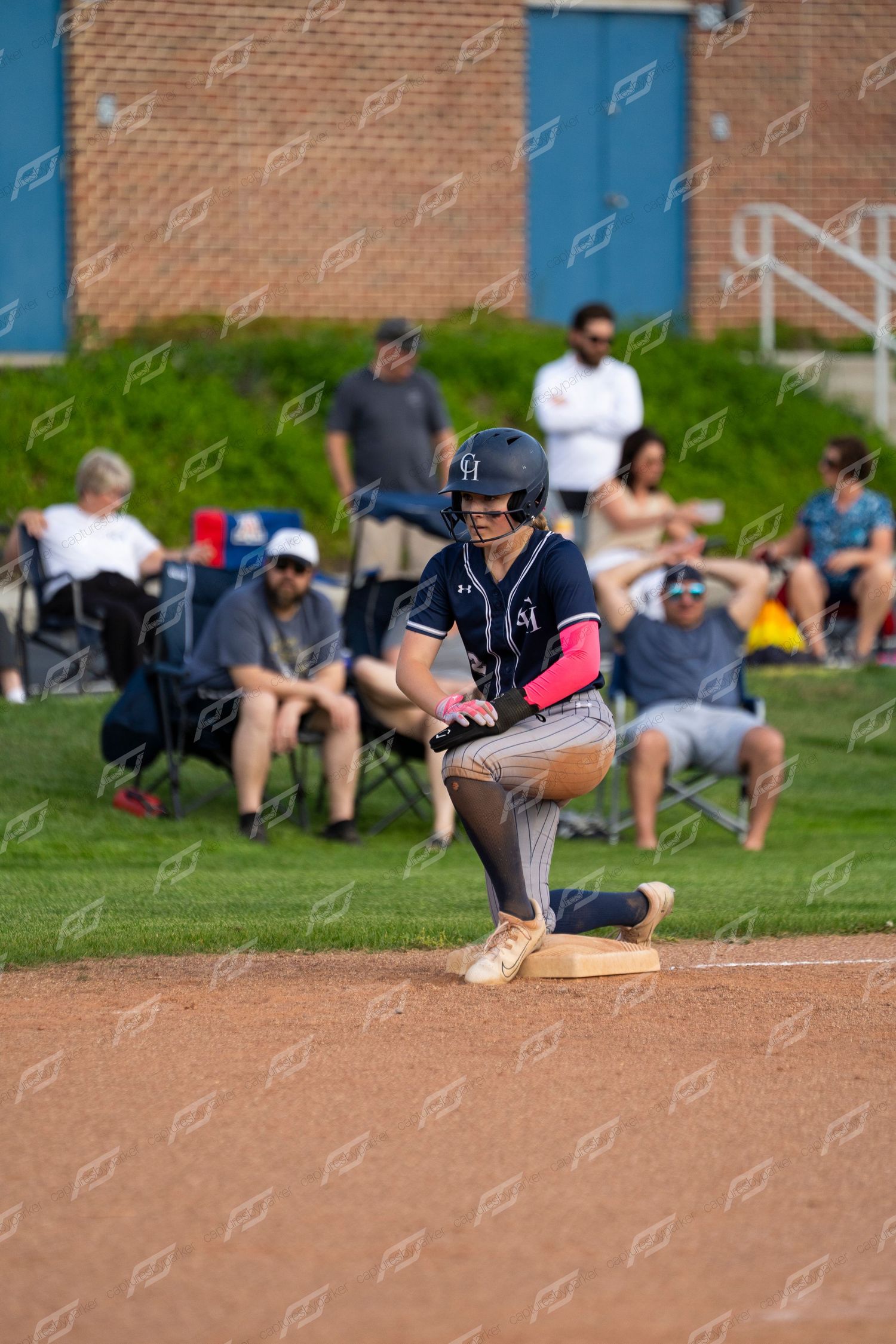 Female softball player in navy pinstripe uniform rounds base during game.