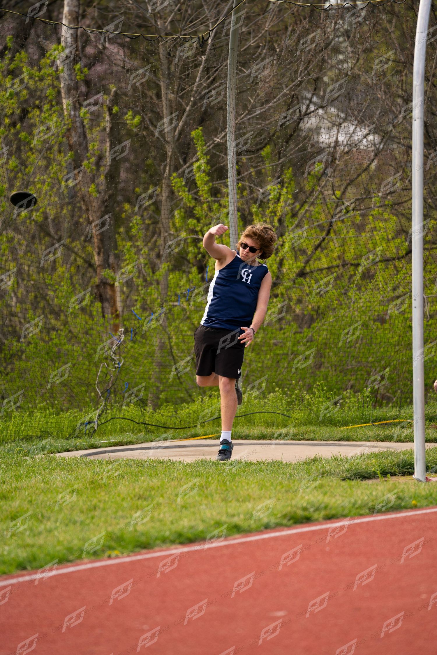 Young male athlete in navy uniform throws a discus during an outdoor track and field event.