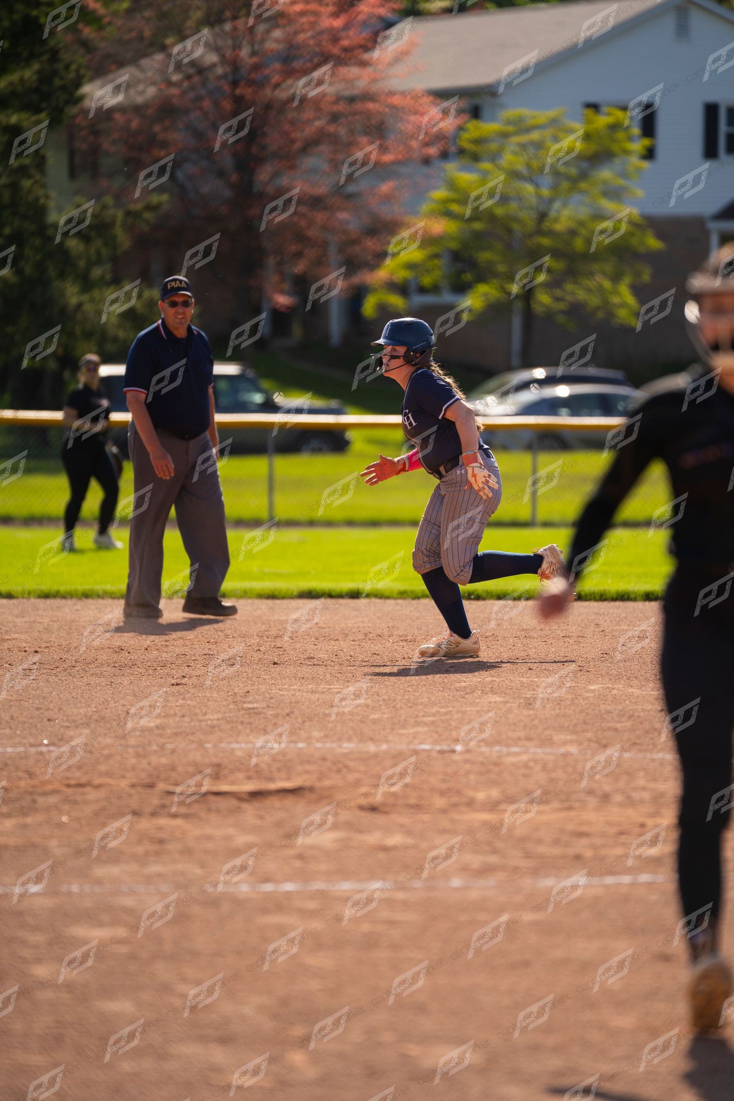 Female softball player rounding second base with an umpire watching during a game.