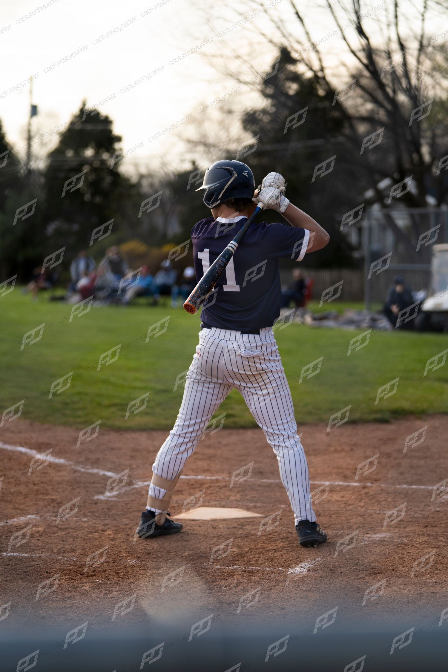 Youth baseball batter #11 in dark pinstripe uniform stands ready at home plate in batting stance.