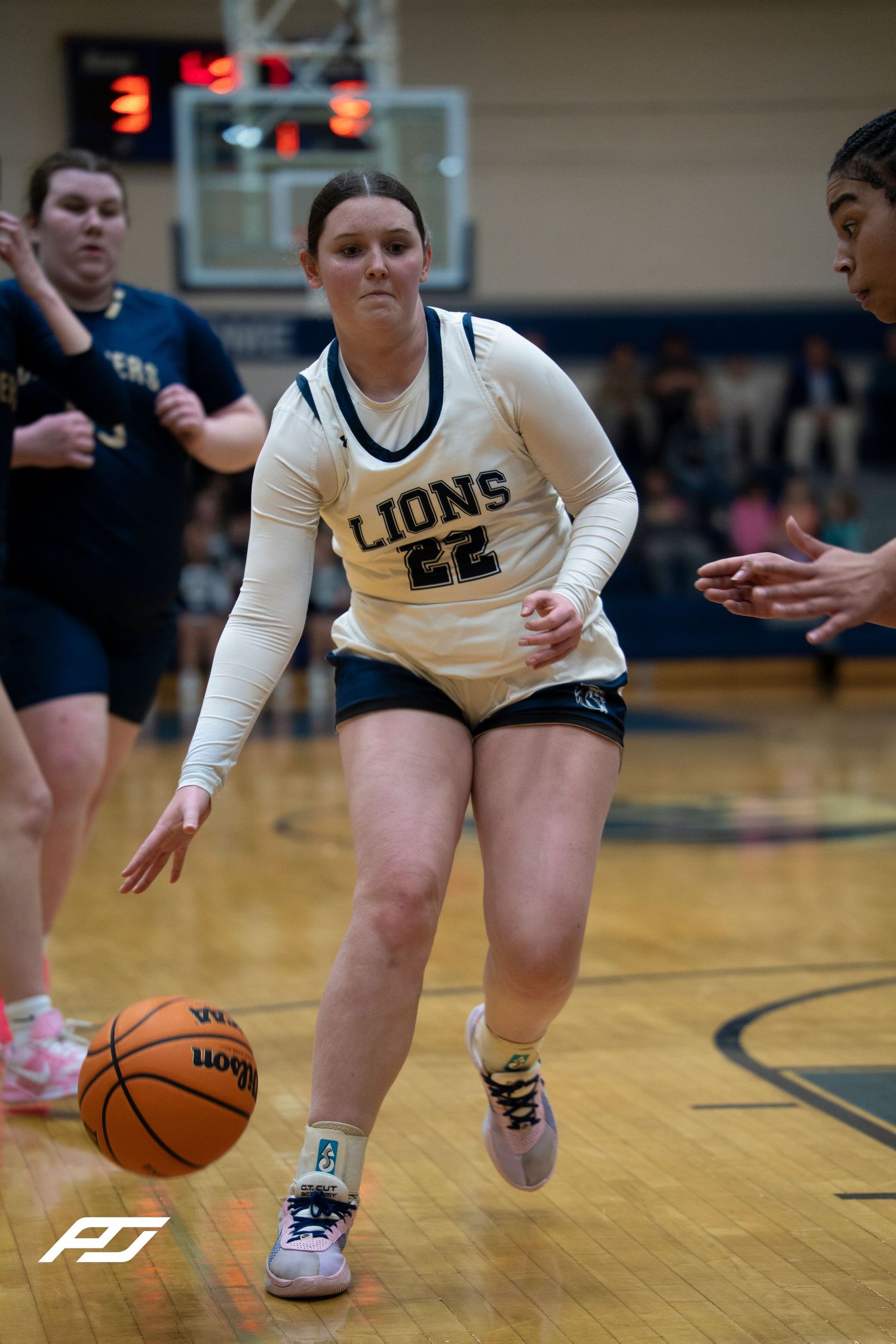 Lions #22 female basketball player dribbles ball aggressively down court during high school game.