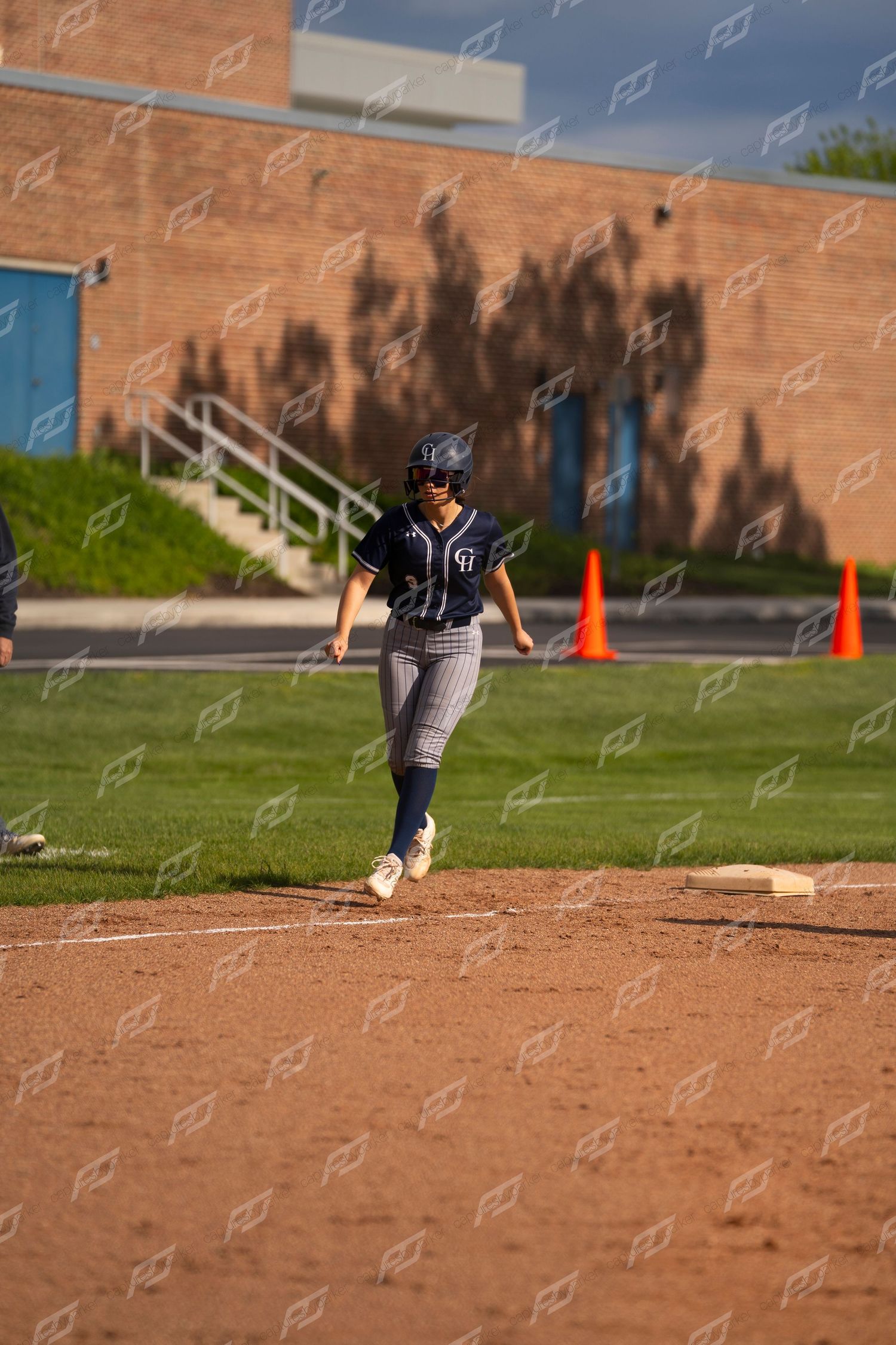 Female softball player in navy uniform approaches a base during a sunny softball game.