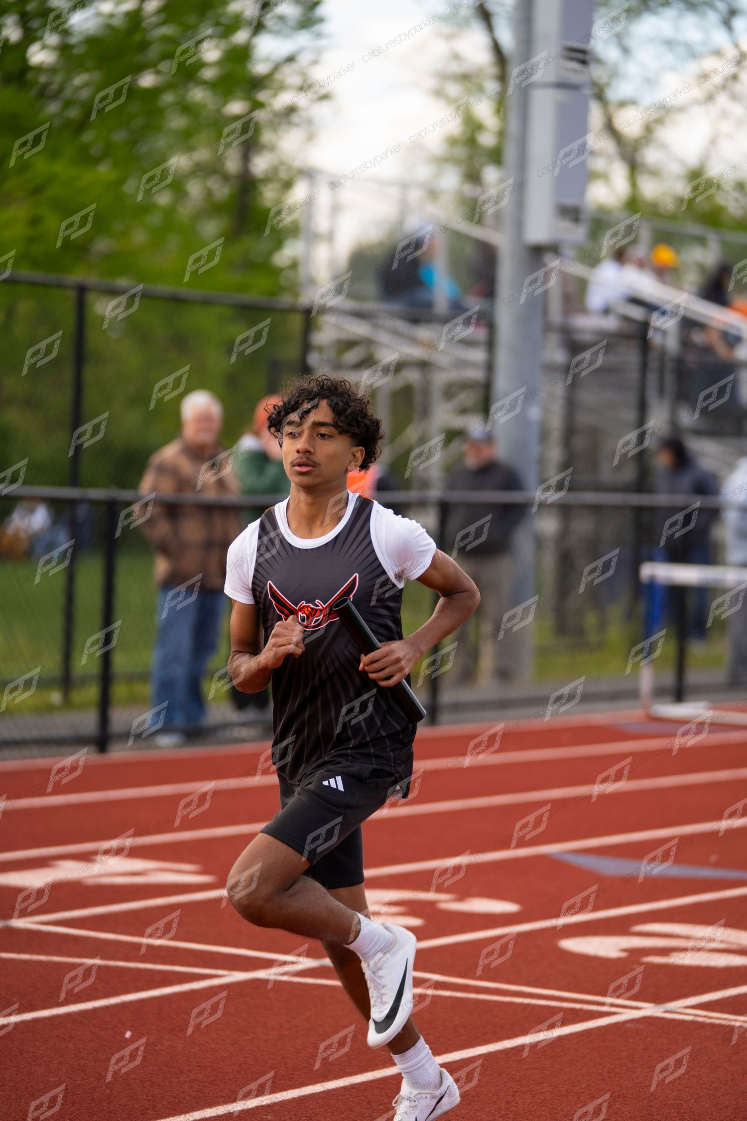 Young male athlete in black uniform running on red track during outdoor track and field meet.