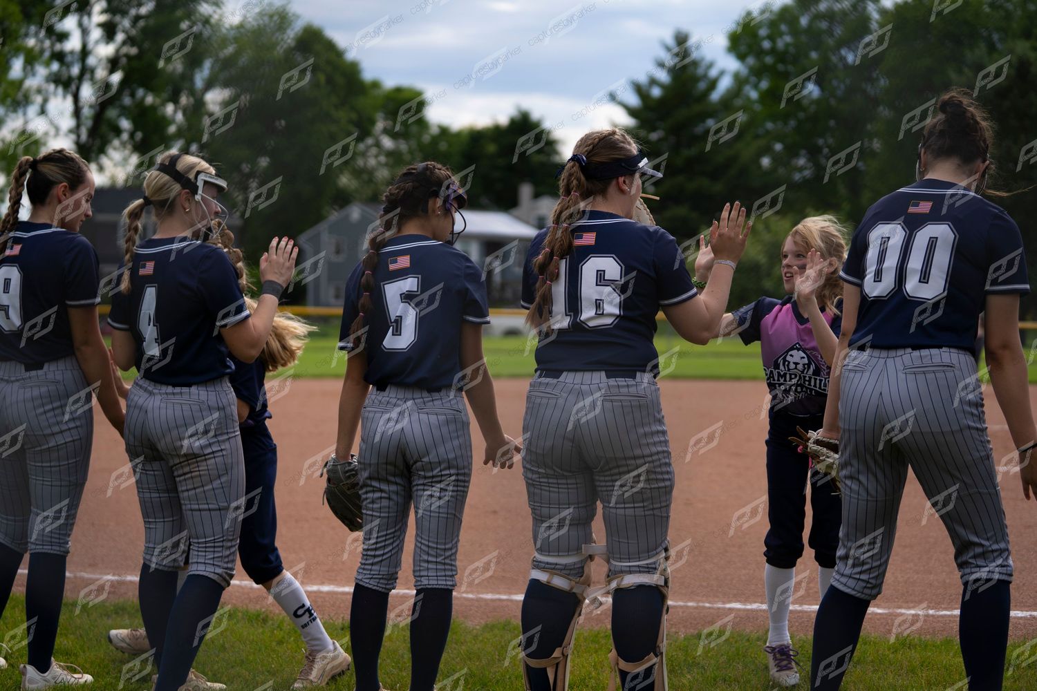 Softball team in navy pinstripe uniforms high-fiving after a game.