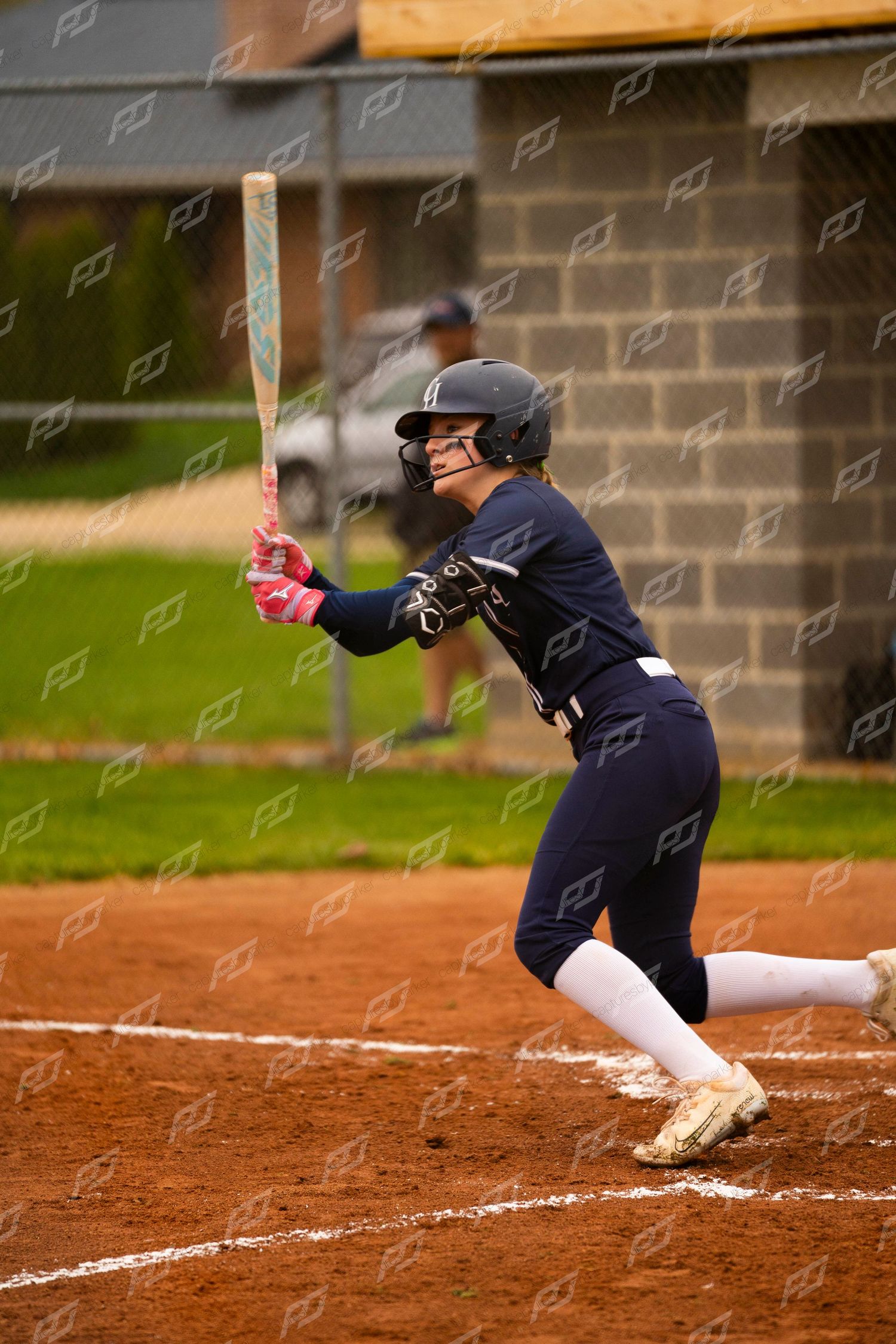 Female softball player in navy uniform and gold cleats prepares to swing the bat.