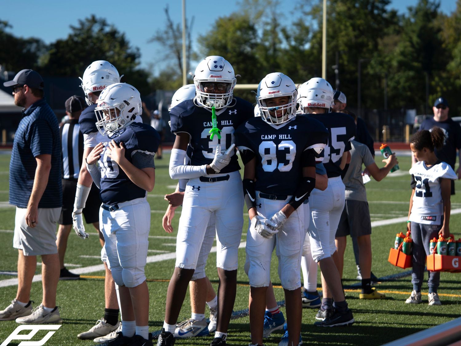 Youth football players in Camp Hill uniforms gather on the sideline during a game.