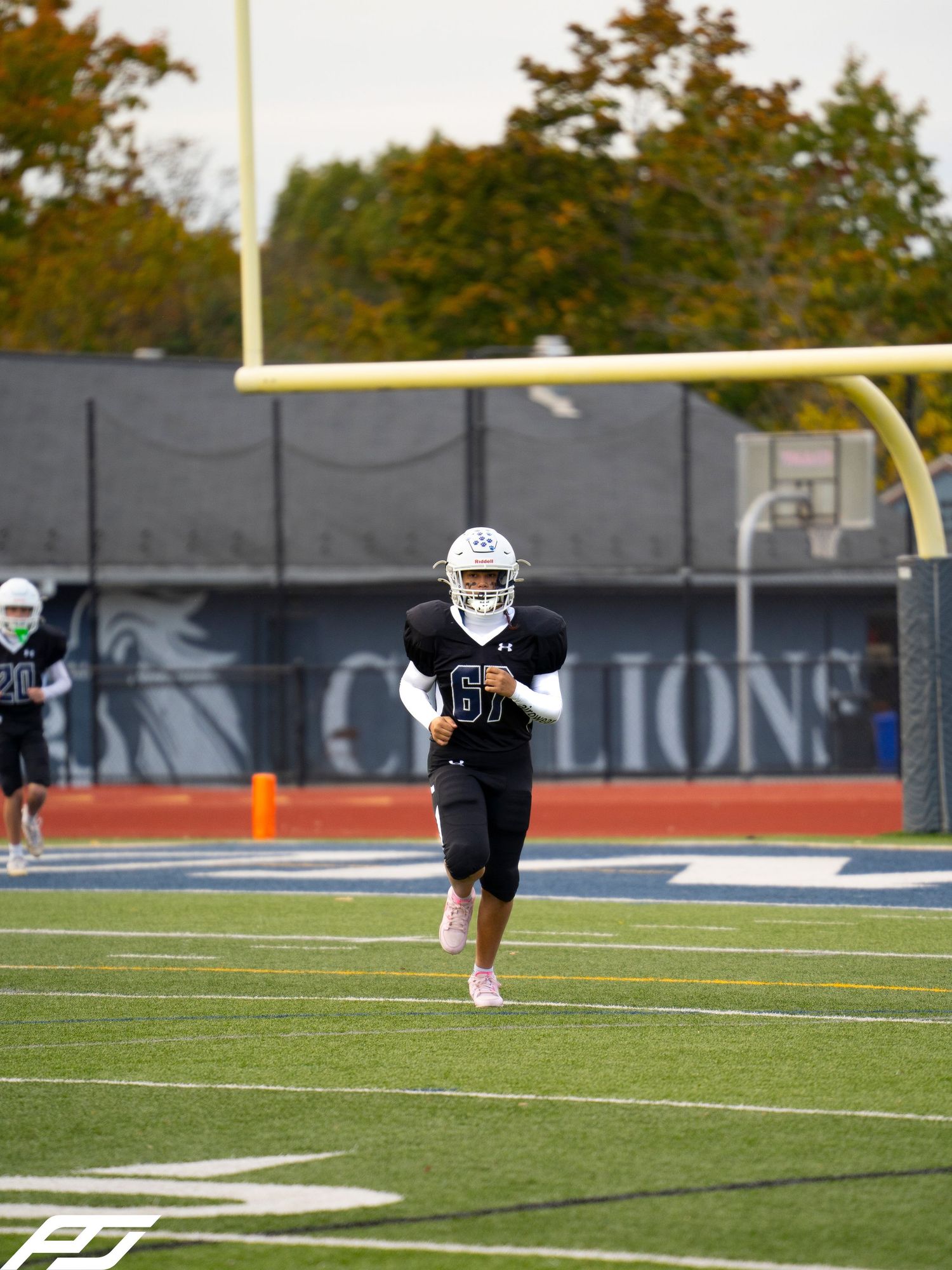 Youth football player #6 in black uniform runs on turf field with goal post behind.