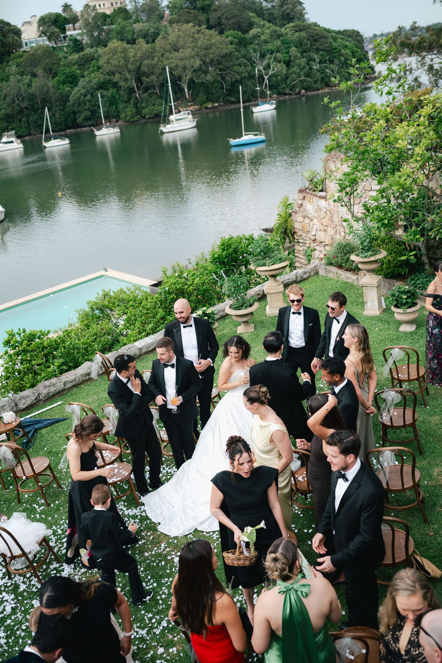 Wedding party gathered on a scenic waterfront terrace with boats in the background.